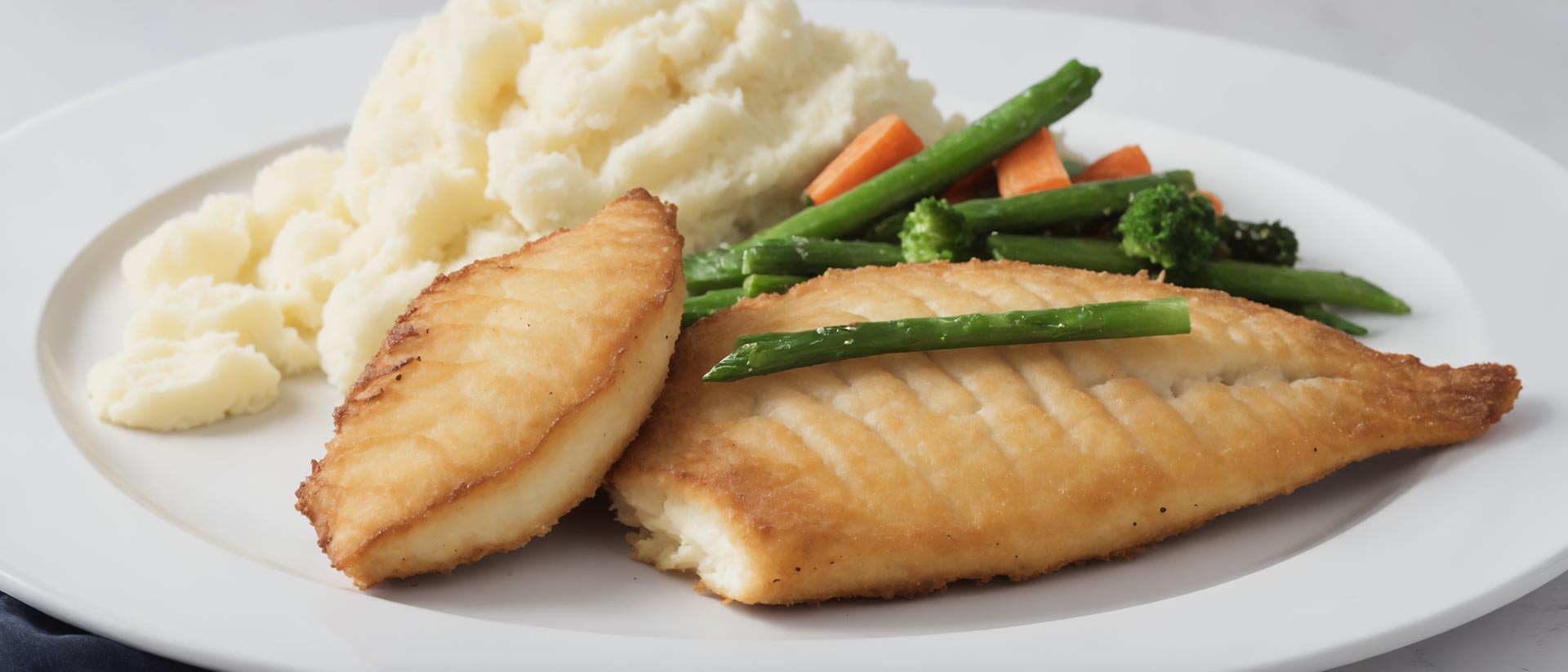 Panierter Fisch auf Teller, als Beilage Kartoffelpüree, dazu Bohnen- und Möhrengemüse